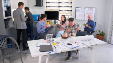 Bir grup insan aile ofisinin konferans odasında bir masada öğle yemeği yiyor. Erkekler ve bayan meslektaşları kahve içer, salata, sandviç ve kek yerler. İş yemeği ya da kahve molası.