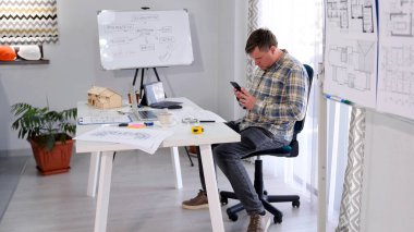 Tasarım mühendisi masasında oturuyor ve cep telefonuyla sohbet ediyor. Şirketin baş mimarı yeni bir inşaat şaheseri üzerinde çalışıyor. Masasında planları, bir dizüstü bilgisayarı falan var..