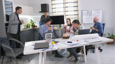 Kahve molası ve iş yemeği. Bir grup insan aile ofisindeki ofis mutfağında bir masada oturuyorlar. Birlikte yemek yiyorlar ve bir proje üzerinde çalışıyorlar..