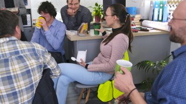 Bir grup mutlu insan ofis mutfağında öğle yemeği yiyor. Arkadaşlar kahve içer ve sandviç yerler. Kahve molası. İş yemeği. Atmosfer rahat ve dost canlısı.