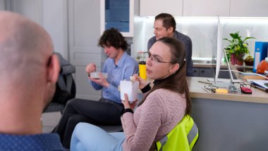 Bir kadın ofis mutfağında iş yemeği sırasında iş arkadaşlarıyla iletişim kurar. Bir grup insan salata yiyor ve konuşuyor. Kahve molası. Bir kadın elinde bir kutu yiyecek tutuyor.