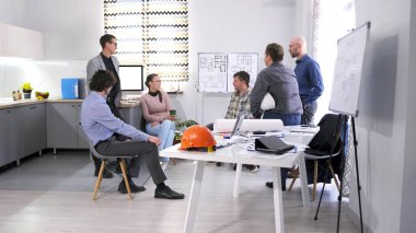 Bir grup müteahhit, mühendis ve işadamı bir konferans odasında fikir ve kavramları tartışıyor. İş birliğinin hakim olduğu atmosfer profesyoneldir.