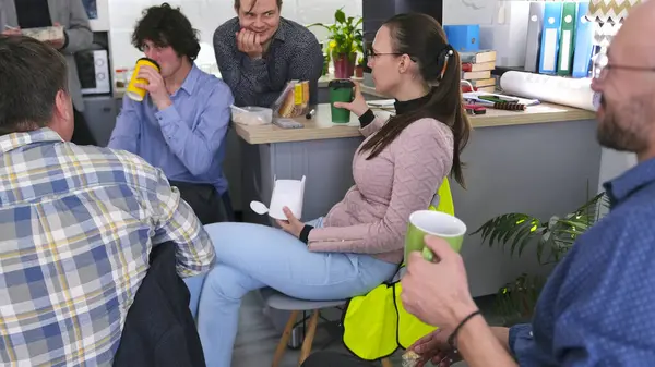 Bir grup mutlu insan ofis mutfağında öğle yemeği yiyor. Arkadaşlar kahve içer ve sandviç yerler. Kahve molası. İş yemeği. Atmosfer rahat ve dost canlısı.