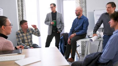 İnşaat şirketinden meslektaşlar, konferans odasında bir toplantı sırasında konuşuyorlar. Bir grup insan projenin detaylarını tartışıyor. Atmosfer ciddi ve odaklanmış görünüyor.