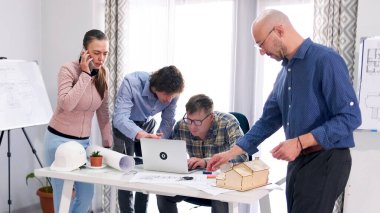 Küçük bir mimarlık şirketi modern bir kır evinin modelini geliştiriyor. Bir grup insan mühendisin masasında birlikte çalışıyor. Bayan sekreter telefonda.