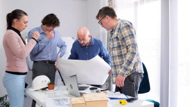 Baş mimarın ofisinde brifing vereceğim. Bir grup iş adamı masanın etrafında toplandı ve büyük bir resmi dikkatle inceliyorlar. Bir inşaat projesini tartışıyorlar..