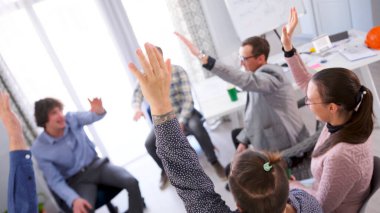 Takım oluşturma etkinliği. Bir grup insan bir konferans odasında ellerini havaya kaldırıyorlar. Sahne pozitif ve enerjik, çünkü insanlar grup aktiviteleriyle meşgul..