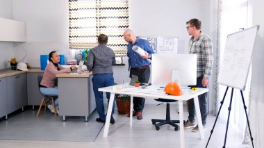 Mimarlık bürosunun aile ofisinde. Bir grup insan inşaat alanının detaylarını koordine etmek için bir konferans odasında toplandı. Atmosfer profesyonel ve işbirliğine elverişli.