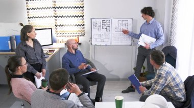 Bir mimarlık şirketinin genç bir çalışanı bir grup insanın önünde bir sunum yapıyor. Sahne odaklanmış ve profesyonel görünüyor, grup bir toplantıda veya tartışmada..