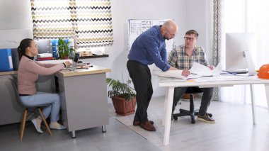 Erkekler rahat bir ofiste mimari bir projeyi tartışıyorlar. Bir işadamı mühendisine talimatlar verir. Şirket personeli binanın inşaat planlarını inceliyor..