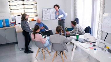 Elinde beyaz bir rulo kağıt olan genç bir adam projenin izleyicilere karlılığını kanıtlıyor. İnşaat şirketinden insanlar, sunum için konferans odasında üzerinde çizimler olan bir tahtanın etrafında toplandılar..