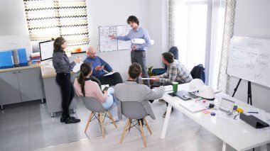 Bir mimarlık şirketinin temsilcisi müşteriler için bir sunum yapar. Bir grup insan konferans odasındaki planlarla birlikte bir tahtanın etrafında toplandı. Şirket çalışanları birlikte çalışıyor.