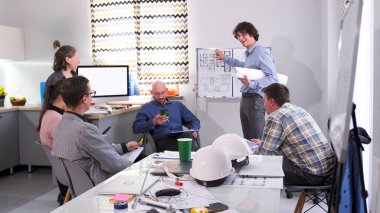 Mimarlardan oluşan mutlu bir ekip, yeni bir mimari projenin sunumunda konferans odasında sohbet ediyor. Bir grup insan, aile ofisinde, çizimleri olan bir adamın önünde toplandı.