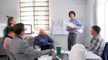 Mimarlık bürosunun gelecek vaat eden genç bir çalışanı bir iş sunumu yapıyor. Bir grup insan öğretim üyesinin etrafında toplandı. Sahne profesyonelce ve işbirliği ruhuyla gerçekleştirilir.