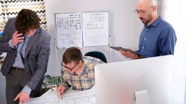 İş adamları mimari bir obje için planlar üzerinde çalışıyorlar. Biri telefonda konuşuyor, diğeri tabletten bir şey izliyor..