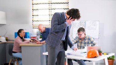 Bir adam cep telefonuyla konuşuyor, inşaat mühendisinin masasında oturuyor. İş adamı belgelere ve çizimlere bakıyor. Mimarlık Bürosu 'nun ofisi. Odadaki diğer insanlar görevlerini yapıyorlar..