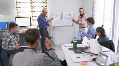 Sunum. Mutlu mimarlardan oluşan bir ekip bir inşaat projesi üzerinde çalışıyor. Bir grup insan, konferans odasındaki planlarla birlikte bir tahtanın etrafında toplandı..