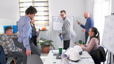 Mimarlık bürosunun rahat ofisinde sunum yapma fikri. Bir grup iş adamı beyaz bir kurulun etrafında çizimler yapıp fikirleri tartışıyor. Sahne ortada.