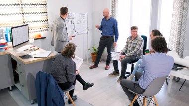 Mimarlar ofisi yeni bir projenin sunumu için toplandı. İki adam çizim tahtasında ders veriyor. Bir grup insan fikirleri tartışıyor ve bilgileri paylaşıyor..