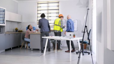 Mimarlık bürosunun çalışanları çizimler ve planlarla standda duruyorlar. Ustabaşı ve tasarımcı projenin detaylarını tartışıyor. Konferans odasında kısa bir brifing. Takım oluşturma