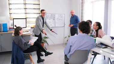 Sabah brifingi. İki adam yeni bir tesisin inşaatı hakkında bir sunum yapıyor. Şirket personeli onları konferans odasında dikkatle dinliyor. Takım oluşturma