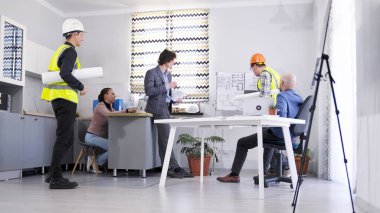 İnşaat şirketinde normal çalışma günleri. İki ustabaşı projenin tahminlerini ve detaylarını koordine etmek için ofise geldi. Bir grup ofis çalışanı bir toplantı odasında çizimlerle birlikte çalışıyor.