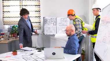 Bir grup adam modern bir iş merkezi kurma planlarını tartışıyor. Müteahhit, ustabaşı ve mühendis çizim tahtasında durur ve patrona bir sunum yaparlar..