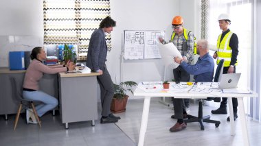 İnşaat şirketinde bir toplantı. Planları olan iki işçi, bir mühendis ve bir tasarımcı inşaat aşamalarını ve proje tahminlerini koordine ediyor. Bir grup insan elinde planlarla bir masanın etrafında dikiliyor.