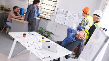 Şef bir öfke nöbeti içinde başını tuttu. İki inşaatçı, bir mühendis ve bir mimar akıllı bir ev için bir plan geliştiriyorlar. Toplantı ya da brifing. Bir adam dizüstü bilgisayarı ve çizimleri olan bir masada oturuyor.