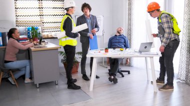 Ustabaşı, inşaatçı ve baş mimarın ofisindeki mühendis projenin tahminini tartıştılar. Bir grup adam elinde planlar ve dizüstü bilgisayarla bir masanın etrafında toplandı. Yorgun patron.