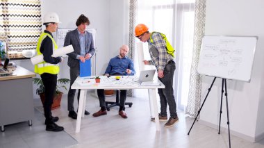 Bir grup adam proje planlarını tartışıyor. İnşaatçı, ustabaşı, mühendis ve mimar toplantı odasında bir araya geldiler. Mimarlık Bürosu. Proje bütçesinin onaylanması