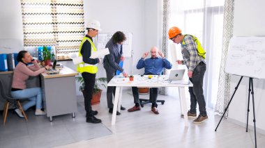 Bir grup inşaat işçisi baş mühendisin masasının etrafında toplandı. Meslektaşlar proje tahminlerini tartışıyorlar. Küçük bir mimarlık bürosunda toplantı. Sahne yoğun ve ciddi.