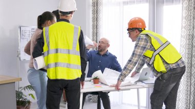 Bir grup inşaat işçisi konferans odasındaki bir masanın etrafında duruyor ve inşaat sürecini tartışıyor. Mühendis astlarına talimat verir. Mimarlık bürosunda brifing.