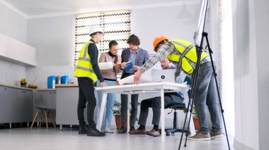 İnşaat şirketinin çalışanları proje tahminini tartışıyor. Yeşil yelekli bir grup işçi inşaat detaylarını baş mimarla koordine ediyor. Takım çalışması.