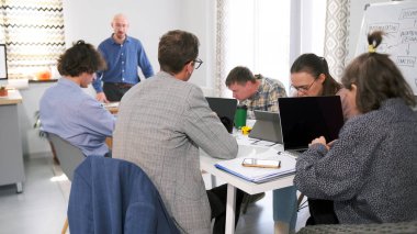 Bir grup ofis çalışanı laptopları açık ve birlikte çalışıyorlar. Herkesin kendi işleriyle meşgul olduğu bir işbirliği ve konsantrasyon ortamı.