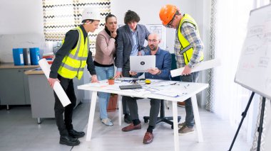 Bir grup insan dizüstü bilgisayar ekranında bir iş binasının çizimlerine bakıyor. İnşaat işçileri, bir mühendis, bir mimar ve bir tasarımcı proje tahminlerini tartışmak üzere masanın etrafında toplandılar.