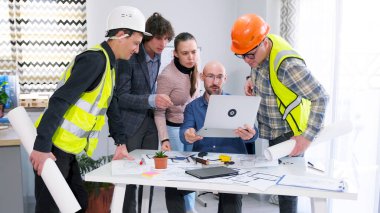 Bir grup işçi mimarın masasının etrafında toplandı ve bir dizüstü bilgisayara bakıyorlar. Proje detaylarını tartışma süreci. Takım oluşturma. Takım çalışması..