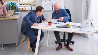 İki başarılı adam proje bütçesini koordine ediyor. Mühendis yapılan iş hakkında patronuna rapor verir. Mimarlık Bürosu. Samimi bir ofiste toplantı. Bilgilendirme