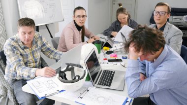 Bir grup mimar dizüstü bilgisayar ve kağıtlarla dolu bir masada oturuyor. Birlikte bir proje üzerinde çalışıyorlar. Takım çalışması ve takım oluşturma. Mimarlık bürosunun çalışma günleri..