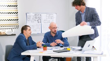 Üç adam planlar ve inşaat planlarını tartışıyor. Mimarlık bürosunun genç bir çalışanı projesini üstleriyle koordine ediyor. Konferans odasında bir grup insan.