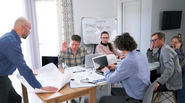 Baş mimar yeni bir iş merkezi inşaatı hakkında brifing veriyor. Bir grup ofis çalışanı toplantı odasındaki masanın etrafında toplandı ve bir proje üzerinde çalıştılar.