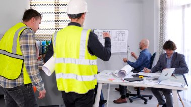 Sorun inşaat sahasında. Koruyucu yelekli ve çizimli bir grup inşaat işçisi mühendislerle aynı masada duruyor. Proje detaylarını tartışacağız. Mimarlık Bürosu