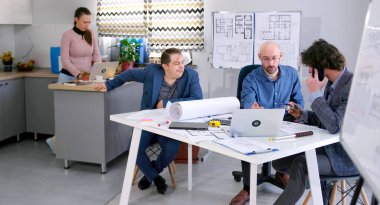 Bir temsilci müşteri projenin bütçesini tartışmak için mimarlık bürosuna geldi. Küçük bir mühendis ekibi modern bir iş merkezinin çizimleri üzerinde çalışıyor.. 