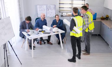 Proje bütçesini çizen iki işçi koordine ediyor. Bir grup adam inşaat detaylarını tartışmak için mimarlık bürosunun rahat ofisinde bir masanın etrafında toplandı..