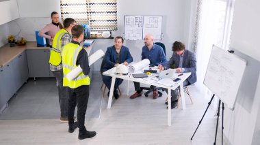 Küçük bir mimarlık bürosunda toplantı. Bir grup iş adamı ve sıradan işçi bir konferans salonunda toplanarak proje planlarını tartıştılar. Sahne odaklı ve ciddi..