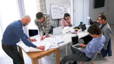 Takım çalışması. Çizimler ve planlar. Gelecek vaat eden bir grup genç toplantı odasında bir masada oturuyor ve modern bir iş merkezi inşa etmek için bir proje üzerinde birlikte çalışıyorlar.