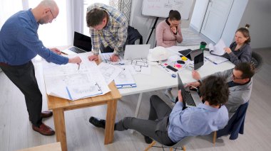 Takım çalışması ve beyin fırtınası. Takım oluşturma. Akıllı ev çizimlerinin geliştirilmesi. Bir grup erkek ve kadın kağıt ve dizüstü bilgisayarlarla bir masada oturuyorlar. Birlikte bir proje üzerinde çalışıyorlar..