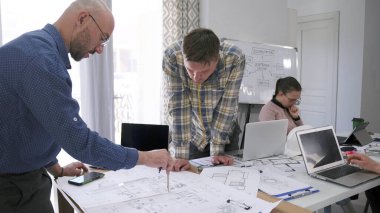 Baş mühendis çizimler üzerinde çalışıyor ve asistanı bina planına dikkatlice bakıyor. Bir adam bir çift pusula ile ölçü alır. Bir mimarlık firmasının ofisi..