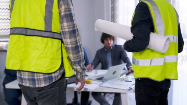 Bir ustabaşı ve elinde çizimler olan yeşil yelekli bir işçi mimarlık bürosunun başkanının masasında duruyor ve maaşlarına zam istiyorlar. İnşaat alanında sorun var. Proje ayrıntılarının tartışılması.