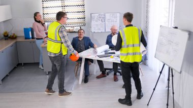 Bir grup inşaat işçisi yönetimle malzeme ve proje çizimleri satın almayı tartışıyor. Mimarlık Bürosu 'nda sabah planlaması. Foreman ve müteahhit